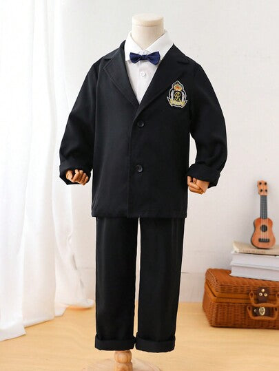 Blazer tweed formel pour jeune garçon avec design à simple boutonnage et décoration d'emblème scolaire, assorti à un pantalon habillé. Convient pour les occasions d'automne/hiver comme les événements scolaires, les fêtes nécessitant une tenue de cérémonie